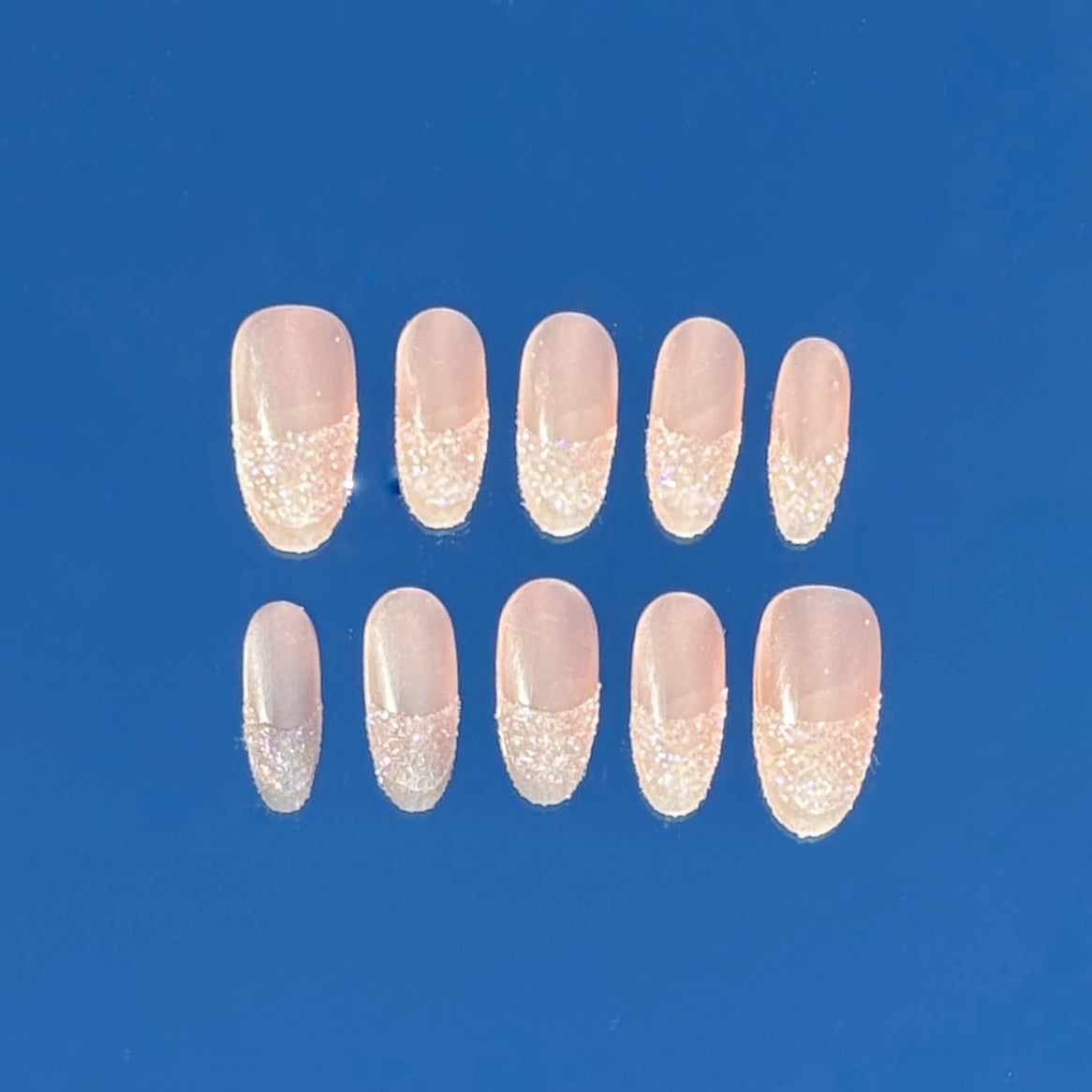 Set of ten press-on nails with glittery tips on a blue background